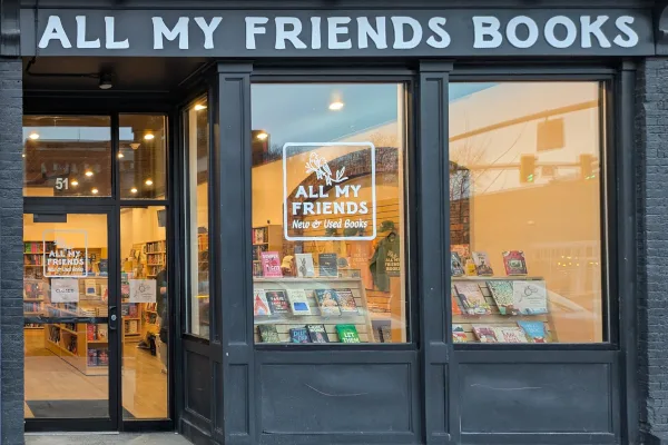 The Cortland shopfront of All My Friends Books at 51 Main Street, its windows lit and full of books
